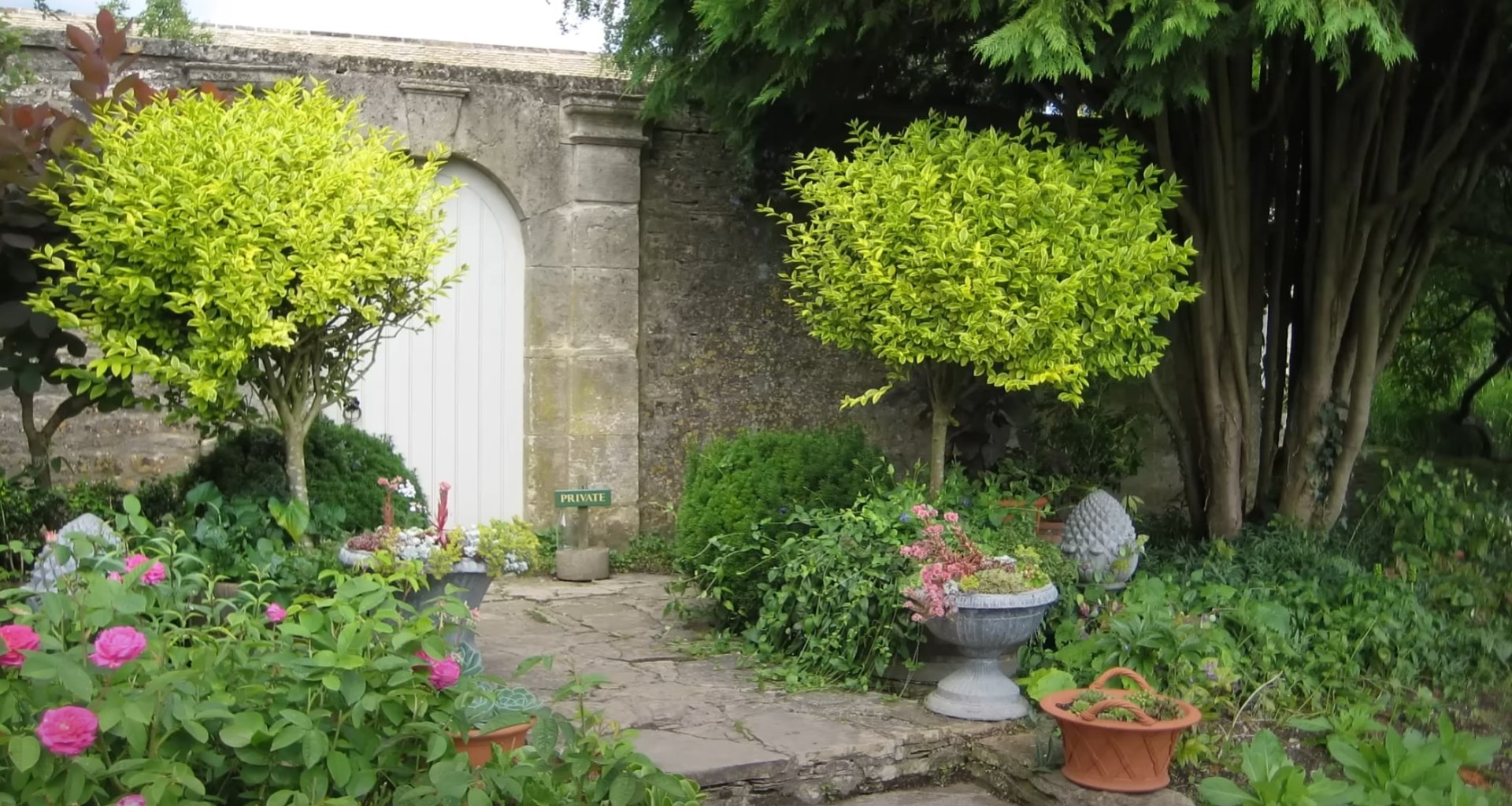Traditional landscape design with stone features and established garden plantings English garden style landscaping with vintage stone archway, decorative planters, and established perennial flower beds