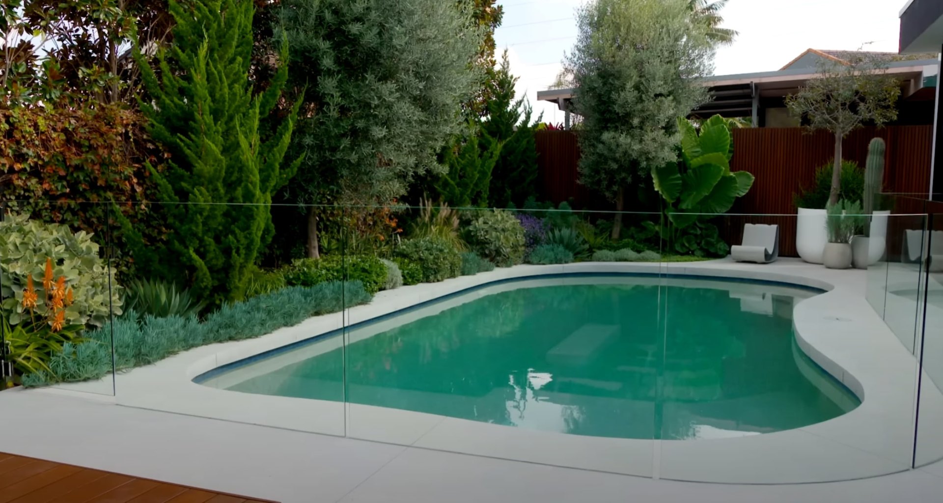 Contemporary landscape design featuring pool area with water-wise plantings Modern backyard landscape design with swimming pool, glass fencing, and drought-resistant plantings